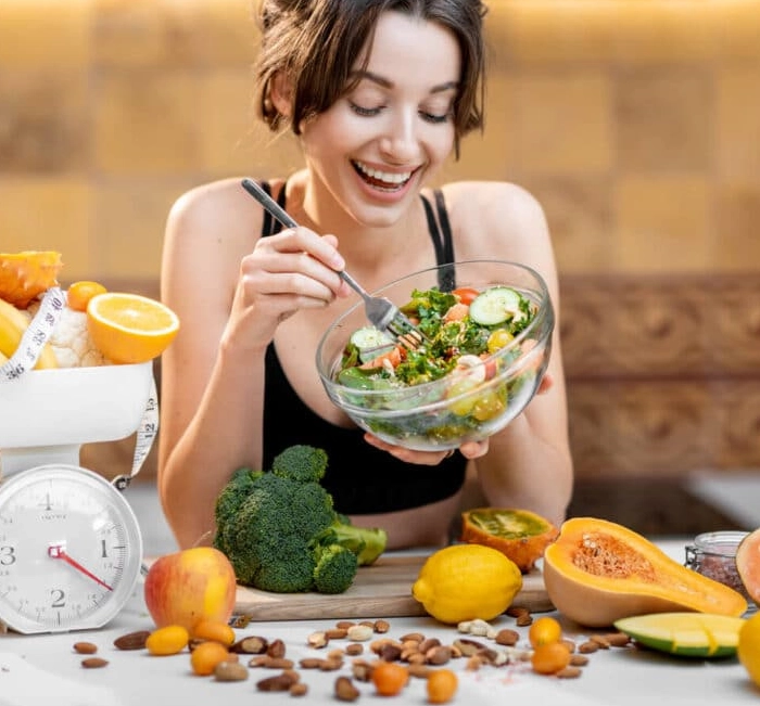 Woman smiling over a bowl of salad next to a scale and measuring tape
