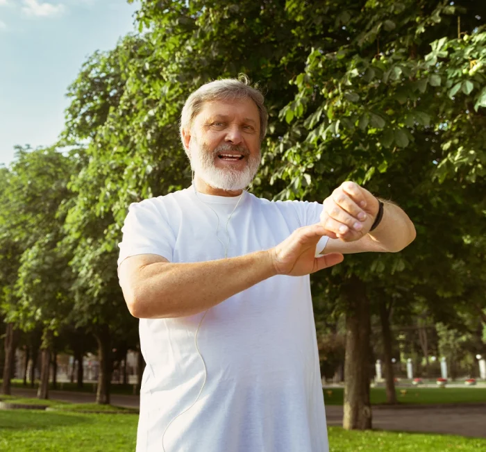 Older man exercising outdoors and checking his fitness watch